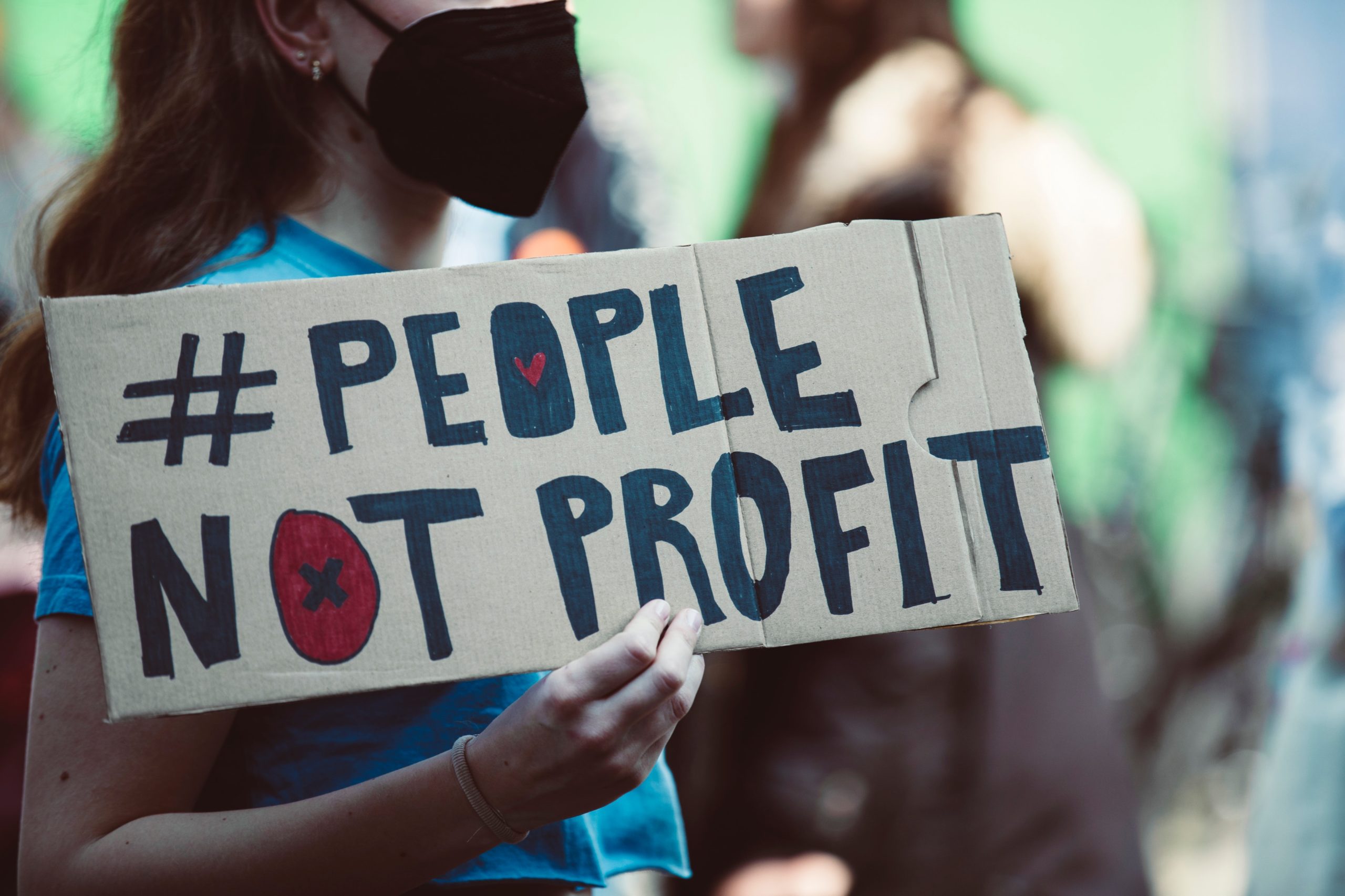 Person holding a sign written on cardboard that reads #people not profit
