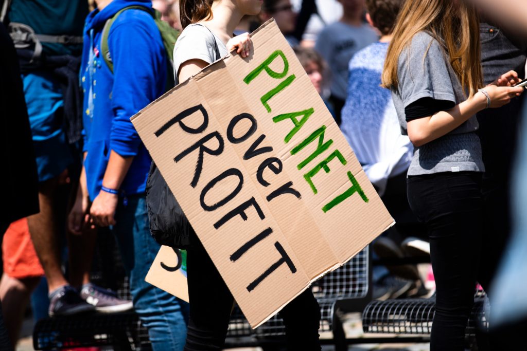 A person at a march holds a sign that reads 'Planet over Profit'