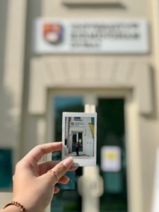 Student holding a polaroid picture of them in front of the campus