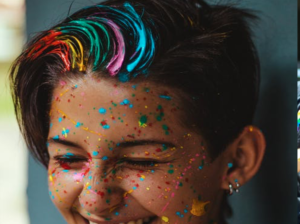 A young person smiling with rainbow coloured hair