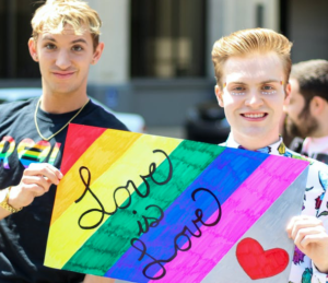 Two young people holding a rainbow coloured sign saying love is love