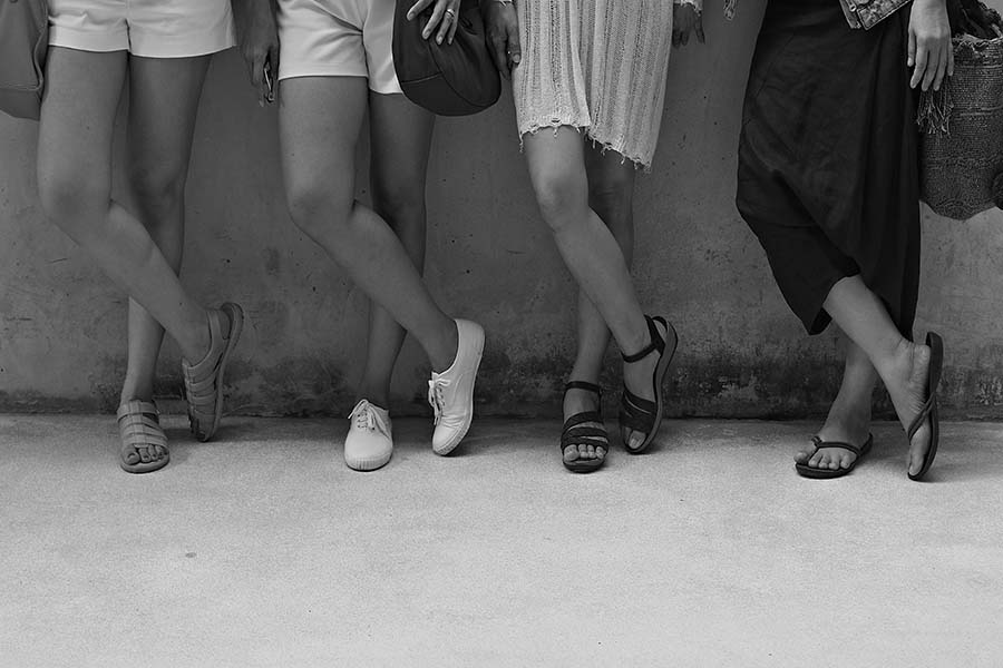 Women standing with cross legs in same position. Black and white picture of women's legs.