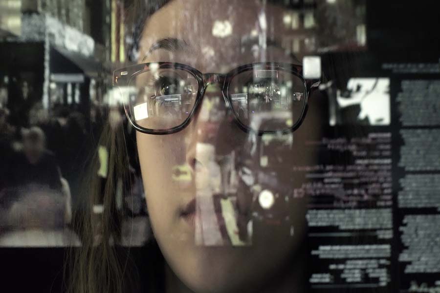 An woman concentrating on a touch screen display. The point of view is from behind the screen, looking through the data & images to the woman's face and hands as she manipulates the windows of information.