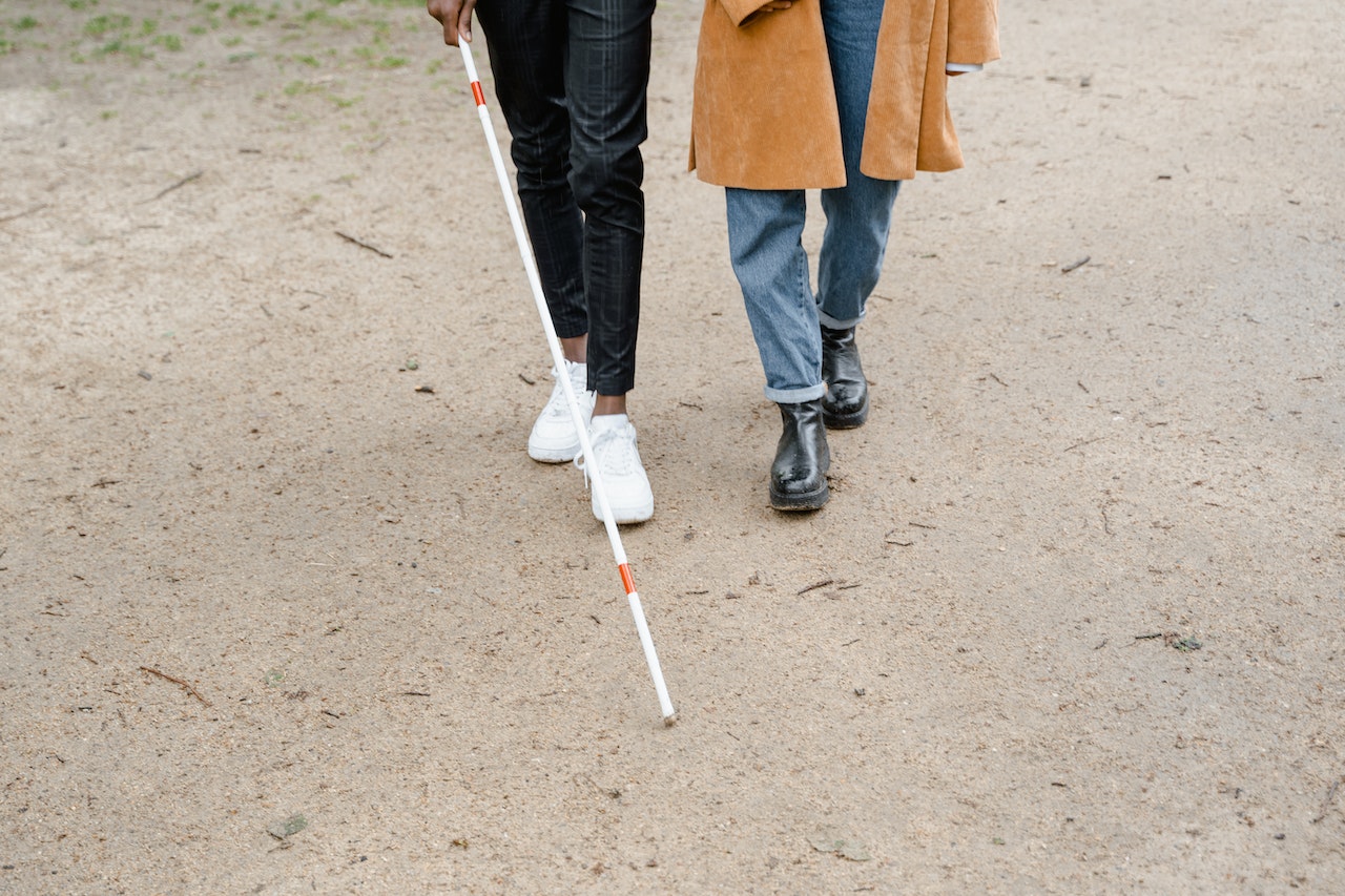 Person walking with another person with a white cane