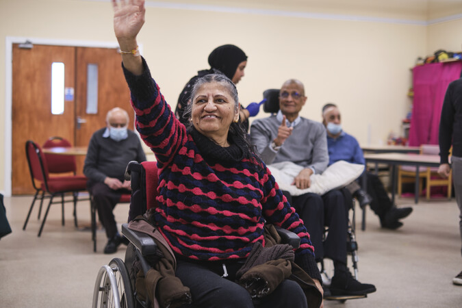 A lady in a wheelchair holds up her arm.