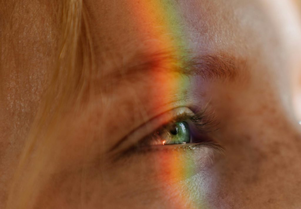 A human's eye with a rainbow light refraction across the face 