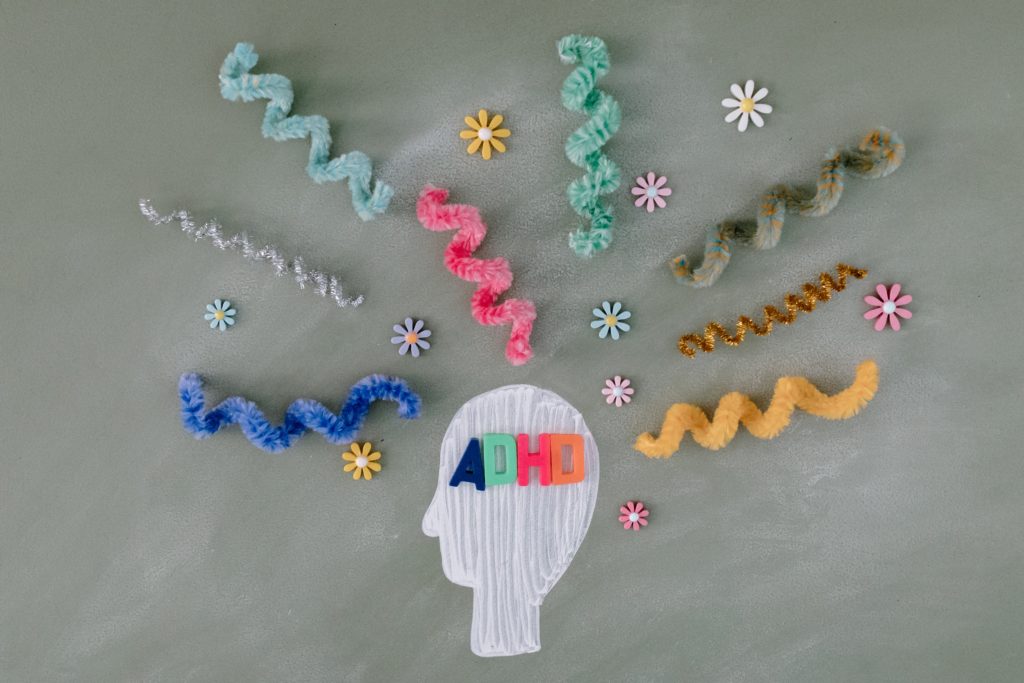 Image shows a drawing of a brain and swiggles made from colourful pipe cleaners coming out of it to represent ideas and thoughts, alongside the word ADHD.