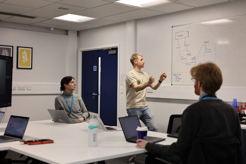 Alex standing in front a whiteboard explaining to others