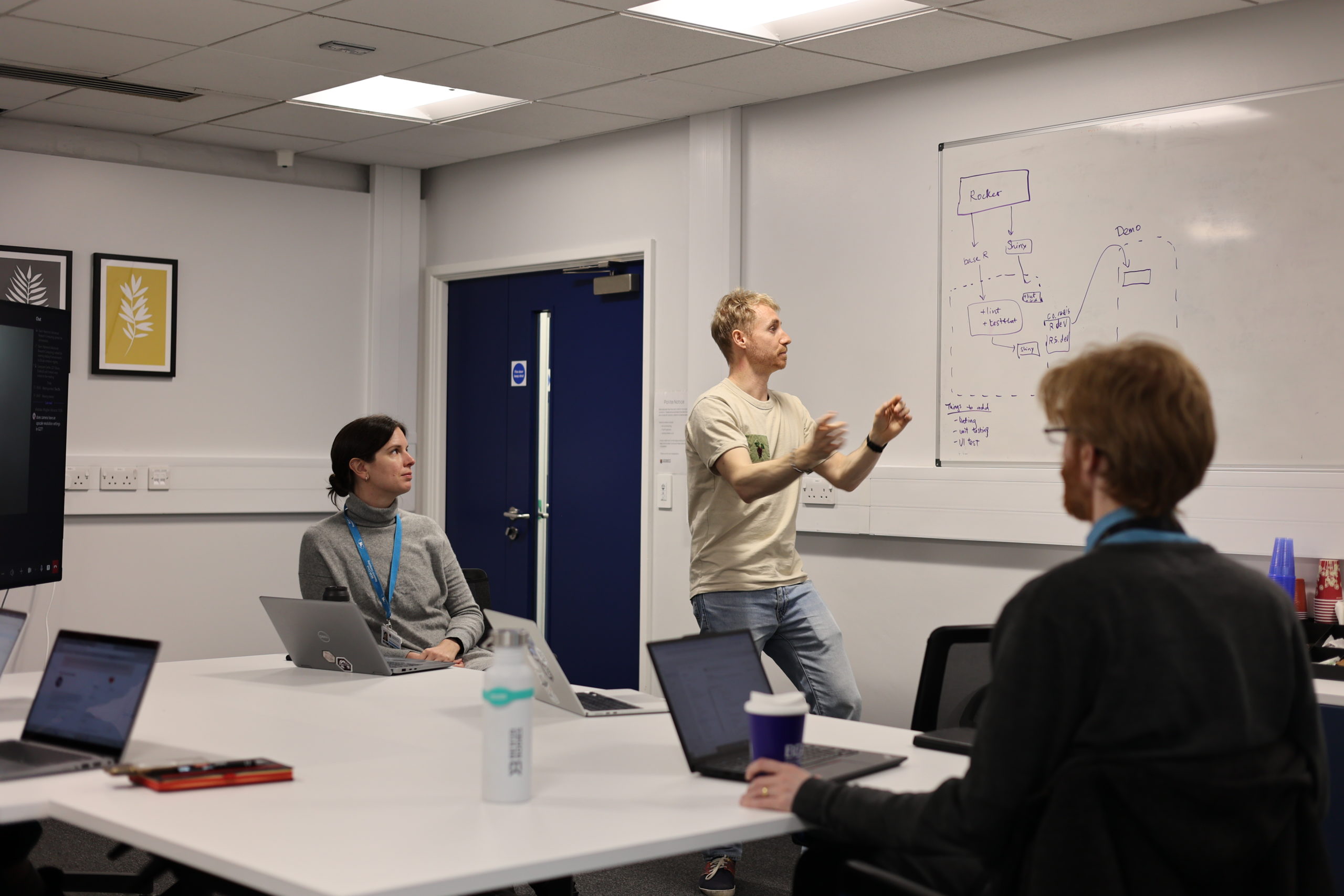 Alex standing in front a whiteboard explaining to others