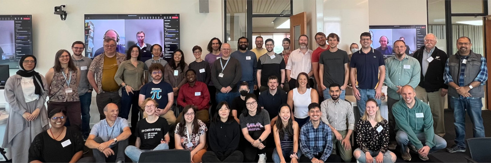 A group photo of around 40 demographically diverse participants at R Project Sprint 2023, including online participants on screen.
