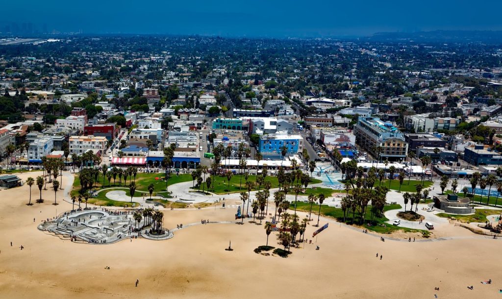 photo of Venice Beach, Los Angeles, showing sand, some grass and trees, and dense urban area