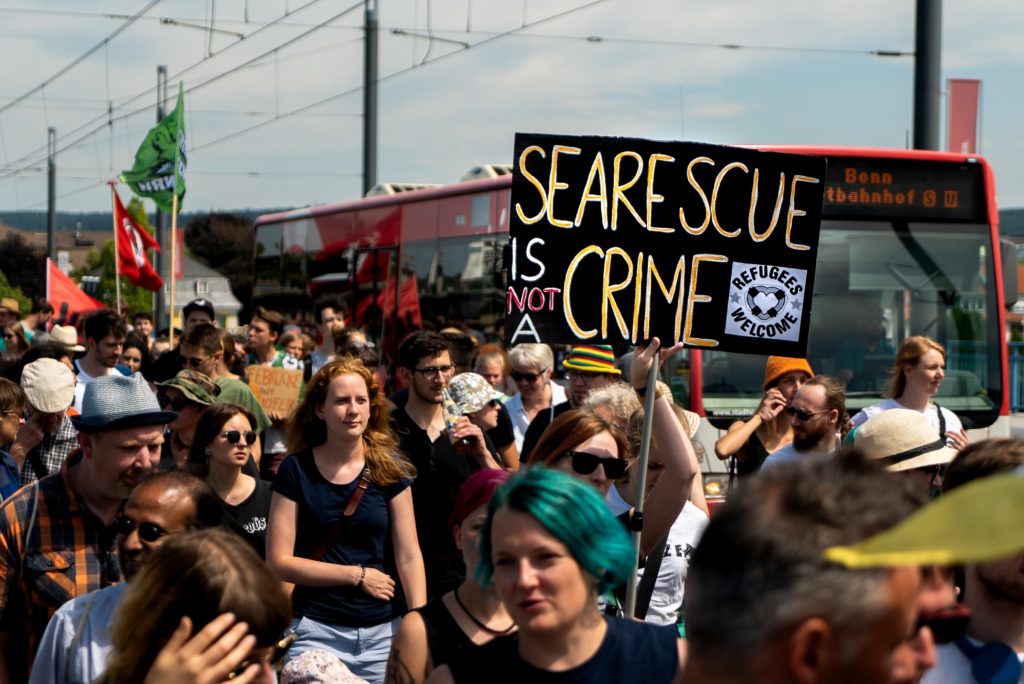 Photo of protest, showing one protester holding a sign saying "sea rescue is not a crime"