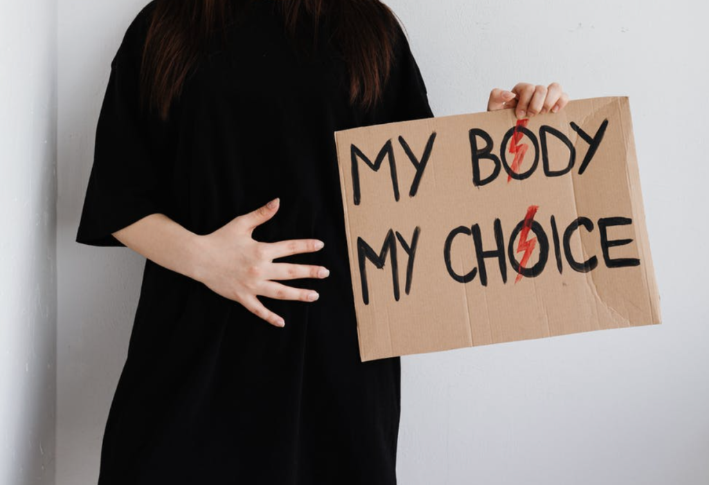 Photo of person who is pregnant, holding a sign saying "my body my choice"