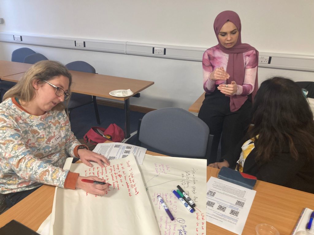 Image shows three women talking and working together on a group activity where they are writing on a large piece of paper with coloured pens. The purpose of the image is to show some of the activities that took place in the training event.